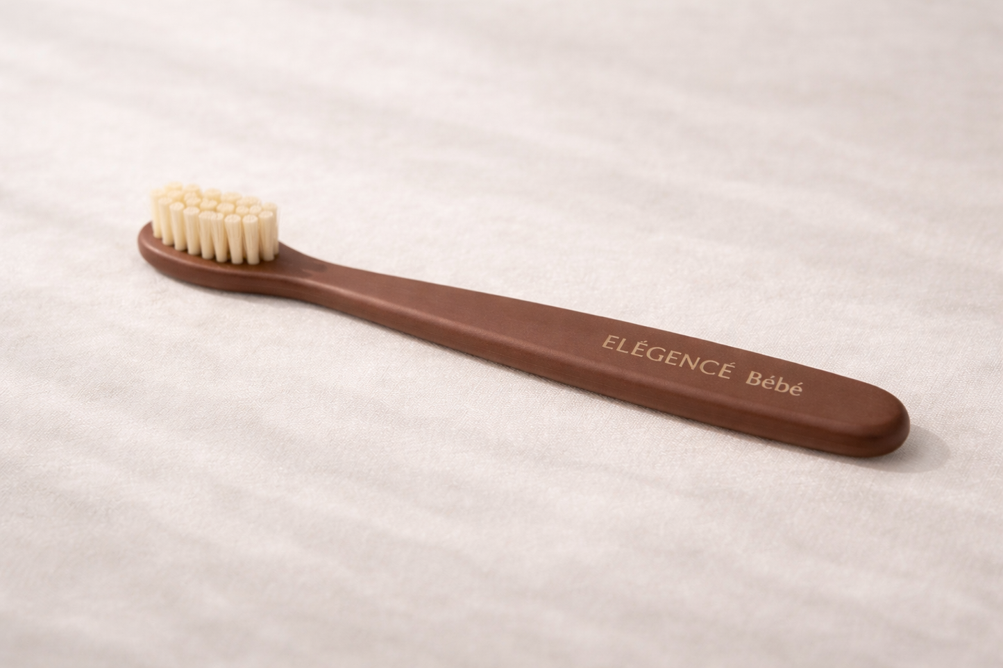Brown baby toothbrush with 'Elegence Bebe' branding on a light background